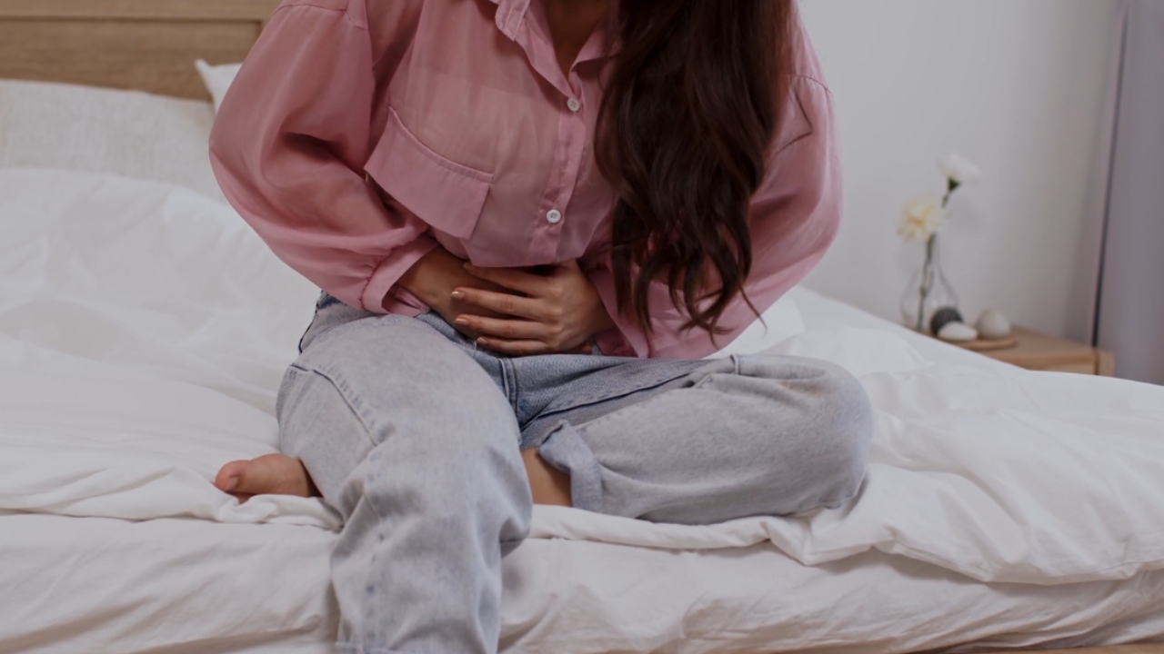 Žena sedi na krevetu i drži stomak zbog jakih menstrualnih bolova